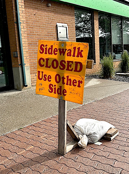 red text of sidewalk closed use other side on yellow sign on interlocking brick sidewalk.