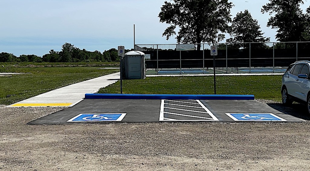 two accessible parking spaces in gravel parking lot next to Amherstburg pickleball courts.
