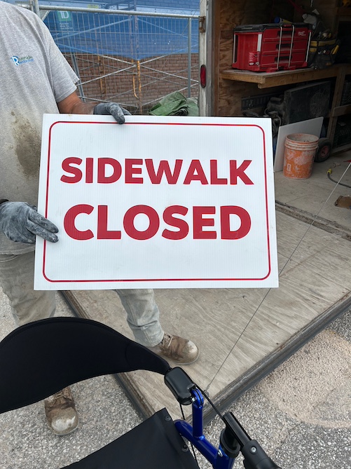 contractor holding sidewalk closed sign in red text on white background